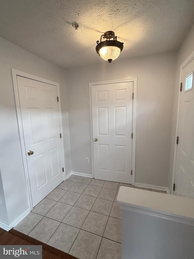 entryway with light tile patterned floors, a textured ceiling, and baseboards