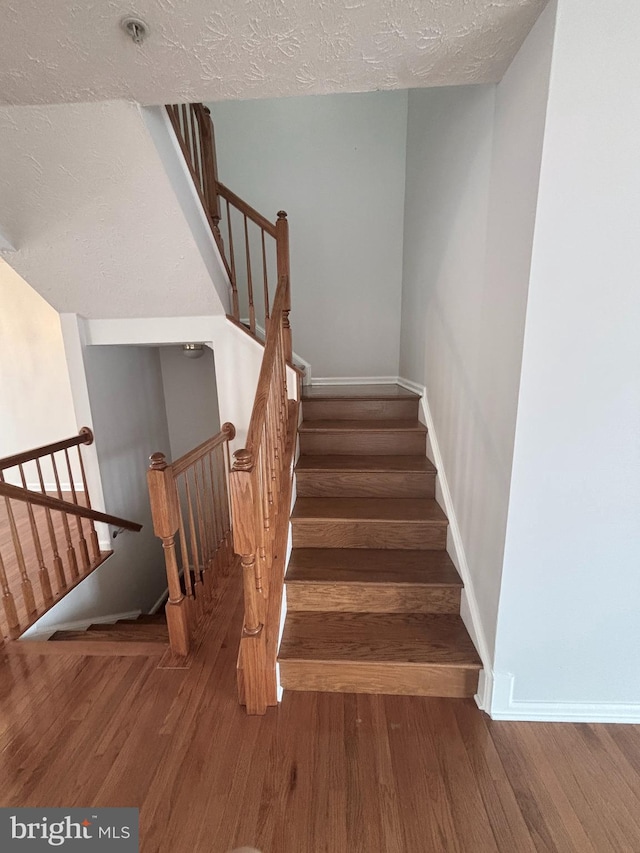 staircase featuring wood finished floors, baseboards, and a textured ceiling