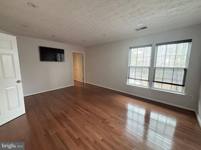 spare room with visible vents, baseboards, a textured ceiling, and wood finished floors