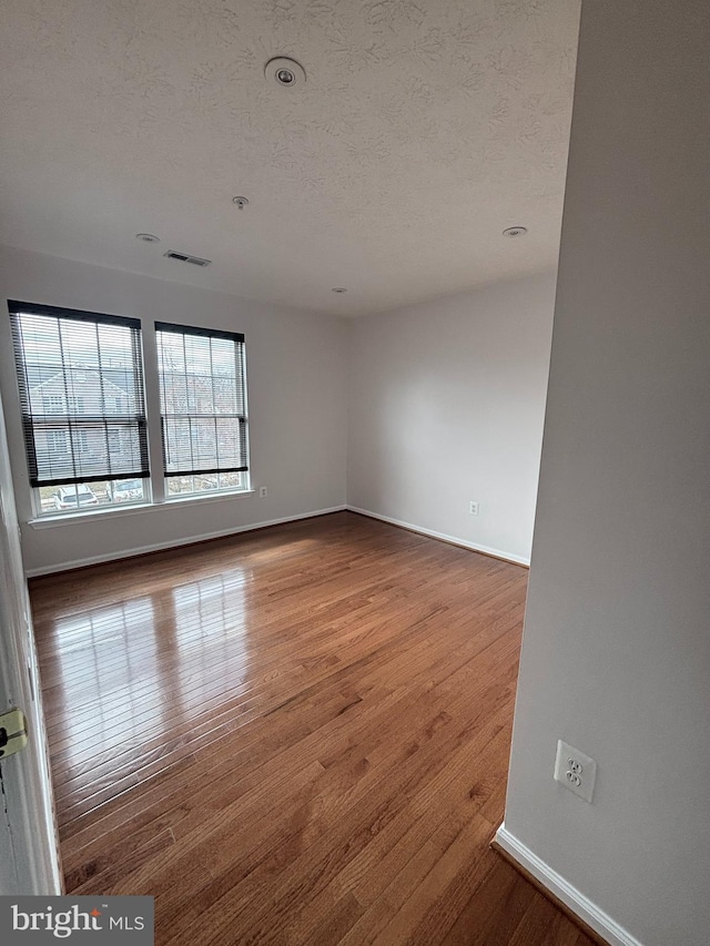 spare room featuring visible vents, a textured ceiling, baseboards, and hardwood / wood-style floors