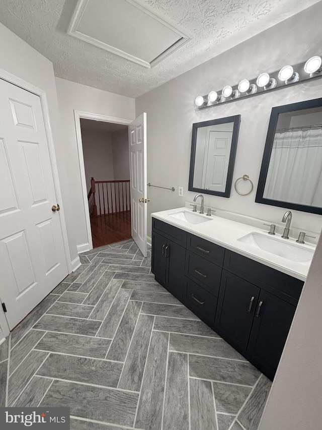 full bath featuring a sink, a textured ceiling, and double vanity