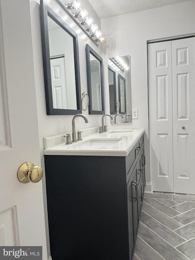 full bathroom with a textured ceiling, double vanity, wood tiled floor, and a sink