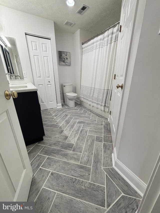 bathroom with vanity, toilet, visible vents, and a textured ceiling