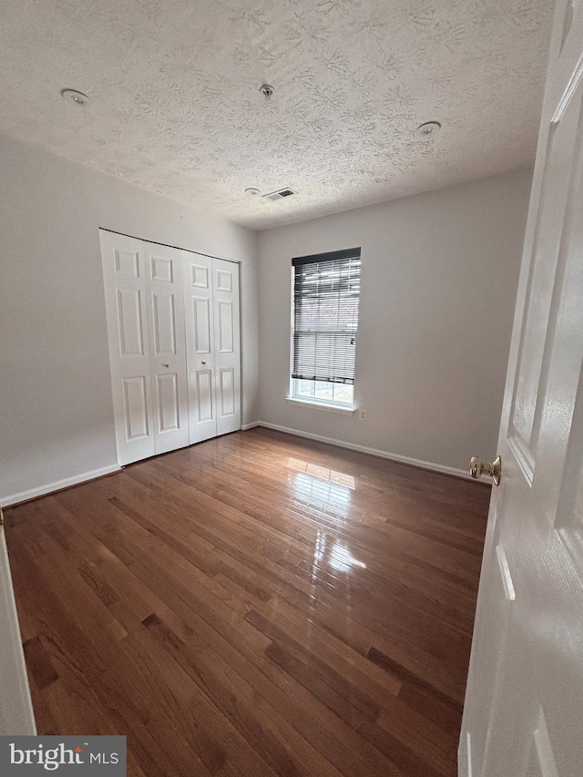 unfurnished bedroom featuring wood finished floors, visible vents, a closet, and baseboards