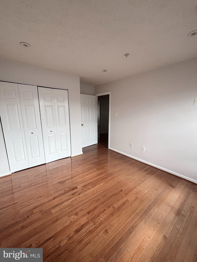 unfurnished bedroom with a closet, baseboards, a textured ceiling, and wood finished floors