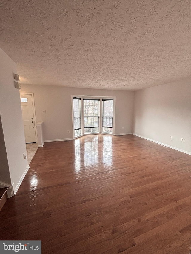 spare room with dark wood-style floors, a textured ceiling, and baseboards