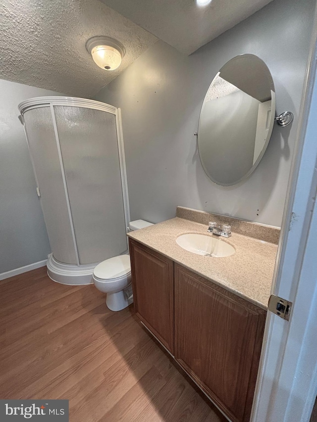 full bathroom with vanity, wood finished floors, a stall shower, a textured ceiling, and toilet