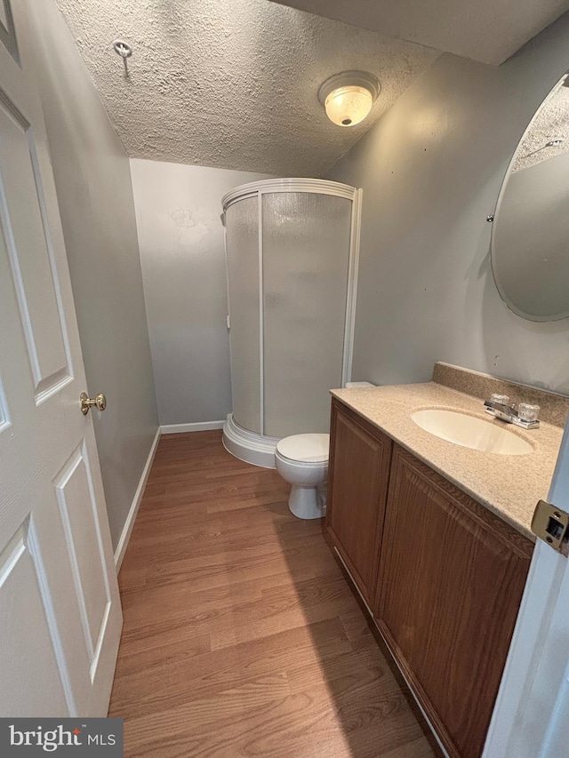 full bath featuring vanity, wood finished floors, a shower stall, and a textured ceiling