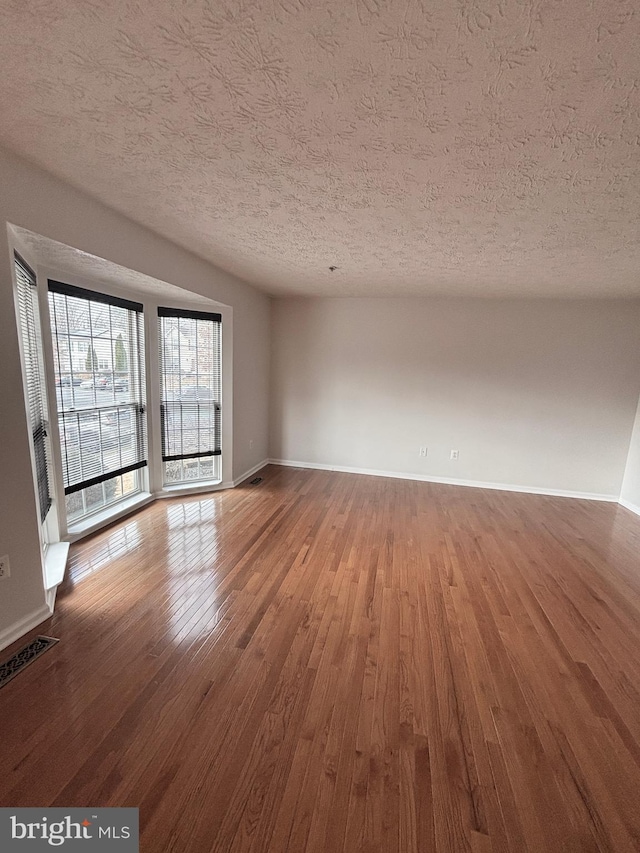 empty room with visible vents, baseboards, a textured ceiling, and wood finished floors