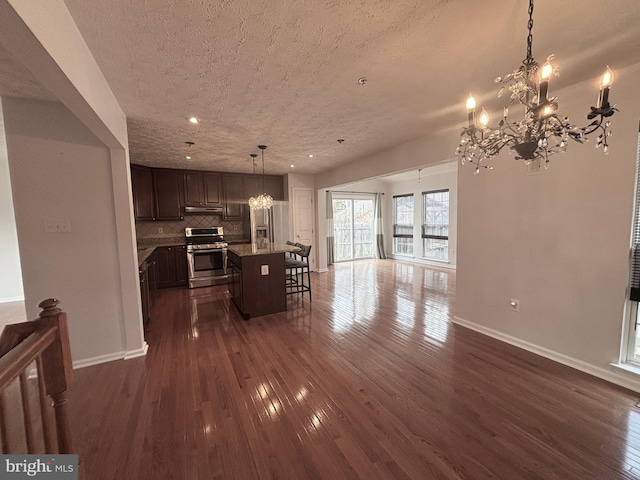 interior space with a notable chandelier, stainless steel range with gas stovetop, open floor plan, and dark wood-style flooring