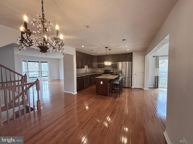 kitchen with dark brown cabinets, stainless steel appliances, dark wood-style floors, and open floor plan