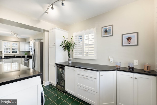 kitchen with stainless steel appliances, dark countertops, beverage cooler, and white cabinets