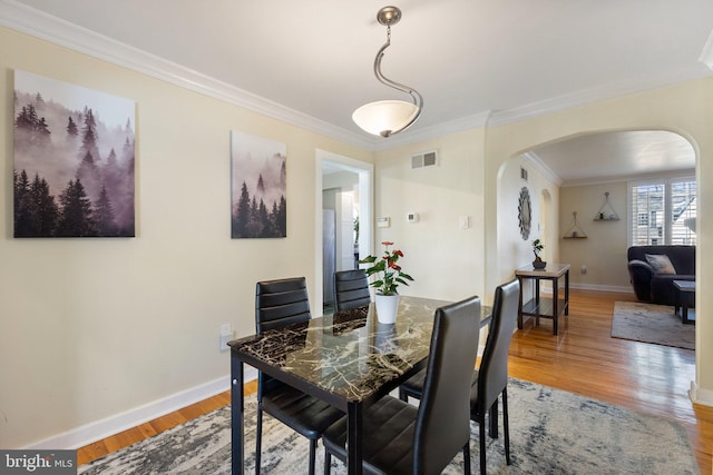 dining room with visible vents, arched walkways, ornamental molding, and light wood finished floors