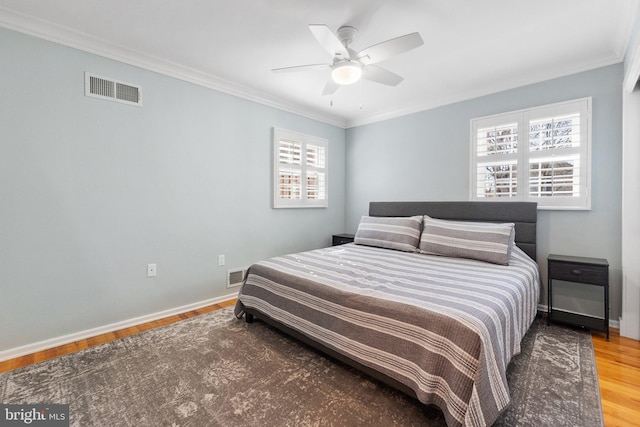 bedroom with ornamental molding, wood finished floors, visible vents, and baseboards