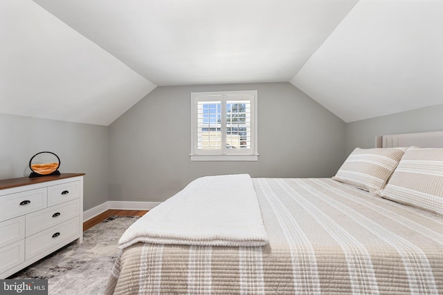 bedroom featuring baseboards, light wood-style flooring, and vaulted ceiling