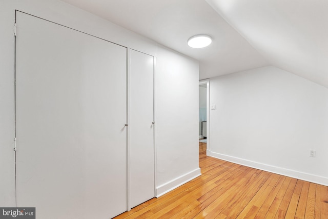 unfurnished bedroom featuring lofted ceiling, light wood-style floors, and baseboards