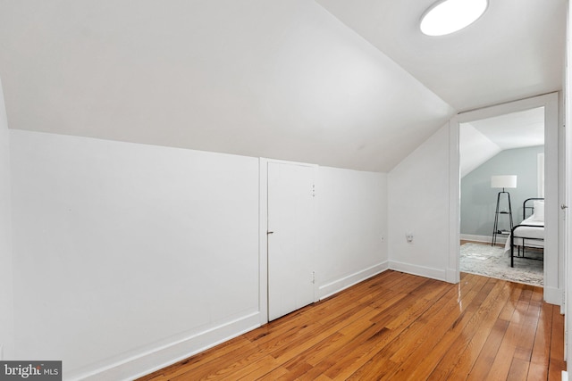 additional living space featuring vaulted ceiling, light wood-style flooring, and baseboards