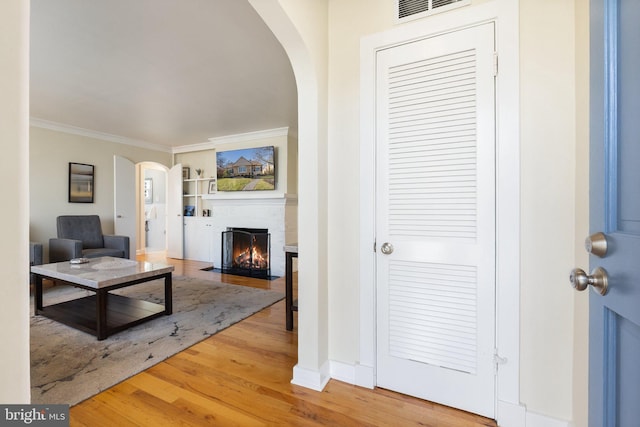 living area featuring visible vents, arched walkways, wood finished floors, and ornamental molding