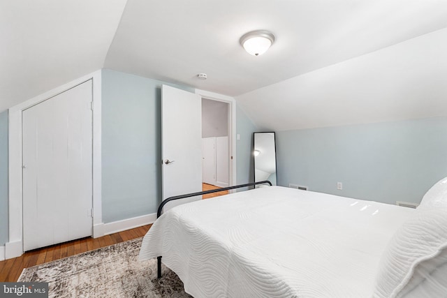 bedroom with vaulted ceiling, wood finished floors, and baseboards