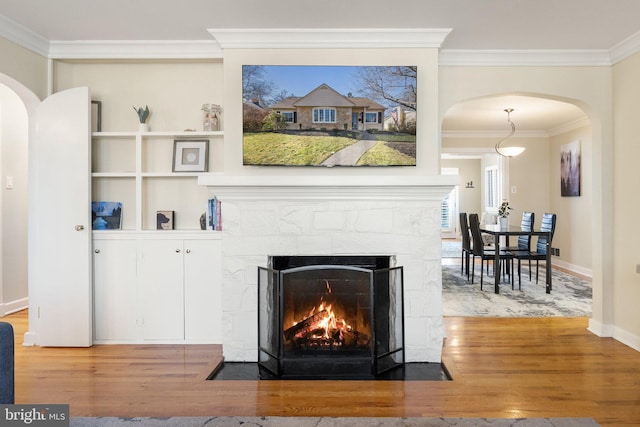 room details featuring a fireplace with flush hearth, ornamental molding, wood finished floors, arched walkways, and baseboards