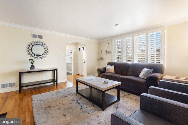 living area featuring visible vents, arched walkways, wood finished floors, and ornamental molding