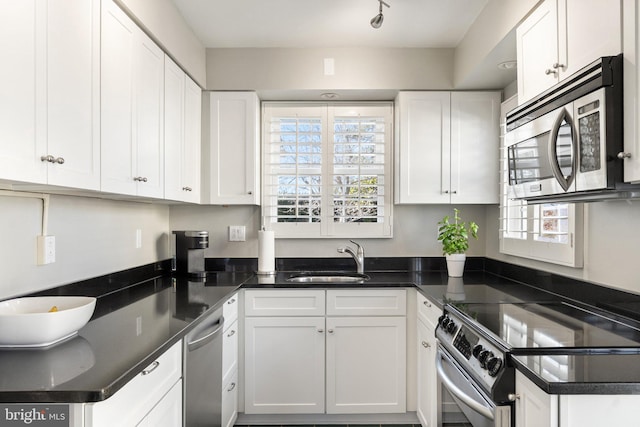 kitchen with a sink, dark countertops, appliances with stainless steel finishes, and white cabinetry