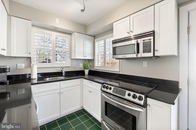 kitchen with dark countertops, white cabinetry, stainless steel appliances, and a sink