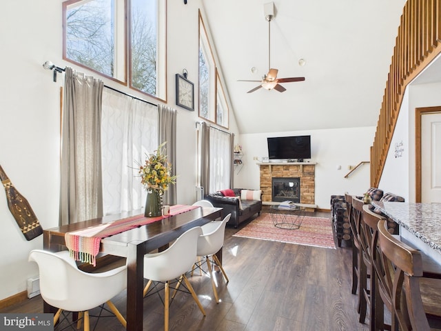 dining area with a fireplace, ceiling fan, dark wood-style floors, and high vaulted ceiling