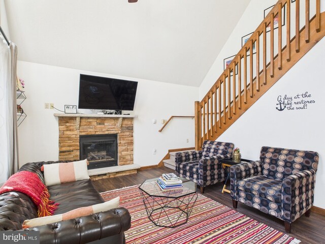 living room with stairs, a stone fireplace, wood finished floors, and baseboards