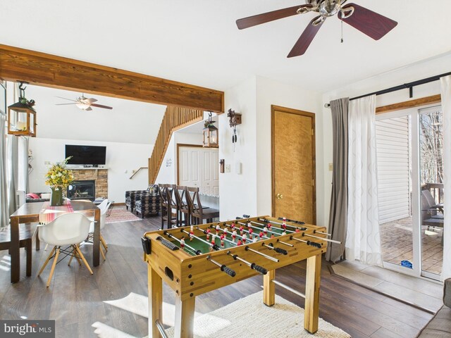 recreation room with ceiling fan, vaulted ceiling with beams, wood finished floors, and a fireplace