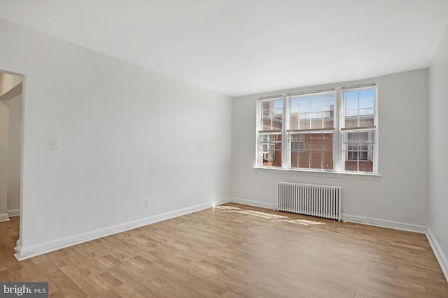 unfurnished room featuring baseboards, wood finished floors, and radiator