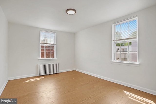 unfurnished room featuring radiator heating unit, baseboards, plenty of natural light, and wood finished floors