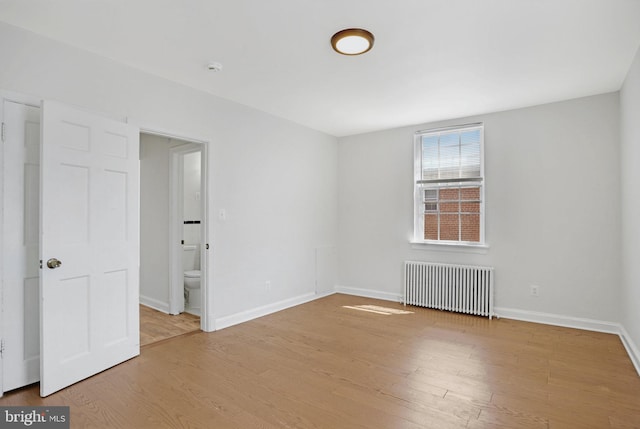 interior space with wood finished floors, baseboards, ensuite bath, and radiator heating unit
