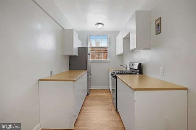 kitchen featuring appliances with stainless steel finishes, light wood finished floors, light countertops, white cabinetry, and baseboards