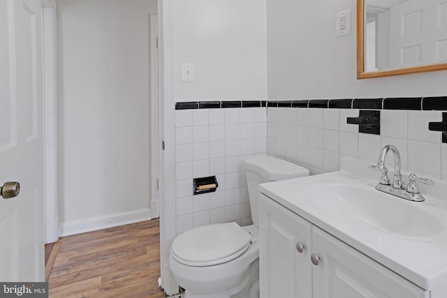 bathroom featuring vanity, toilet, baseboards, tile walls, and wood finished floors
