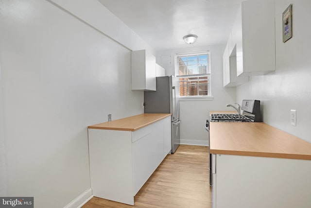 kitchen with appliances with stainless steel finishes, light wood finished floors, light countertops, white cabinetry, and baseboards