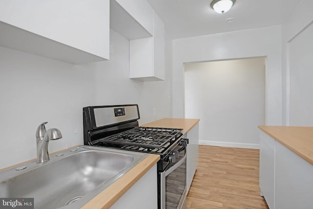 kitchen with stainless steel gas stove, light wood-type flooring, light countertops, white cabinets, and a sink