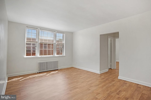 spare room with radiator, baseboards, and light wood-style flooring