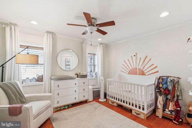 bedroom with recessed lighting, ornamental molding, a crib, and wood finished floors