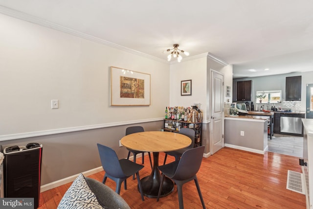 dining area featuring light wood finished floors, visible vents, baseboards, and ornamental molding