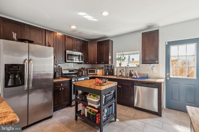 kitchen with a sink, stainless steel appliances, dark brown cabinetry, wood counters, and tasteful backsplash