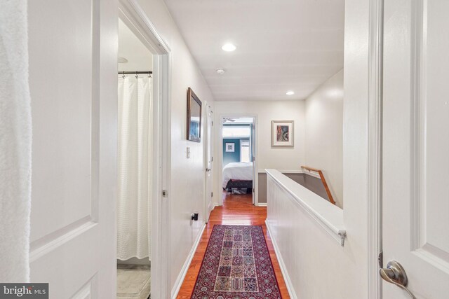 corridor with an upstairs landing, wood finished floors, recessed lighting, and baseboards