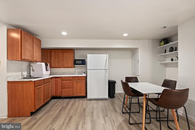 kitchen featuring black microwave, light wood-type flooring, light countertops, freestanding refrigerator, and open shelves