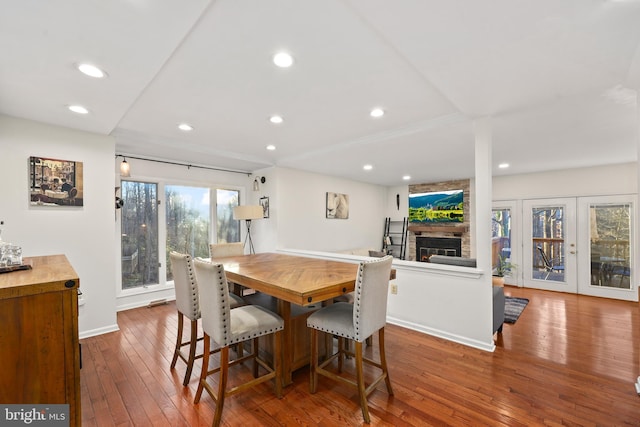 dining space with hardwood / wood-style flooring, recessed lighting, french doors, a large fireplace, and baseboards