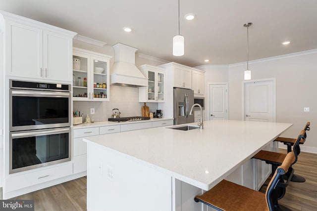 kitchen featuring custom range hood, a sink, wood finished floors, stainless steel appliances, and decorative backsplash