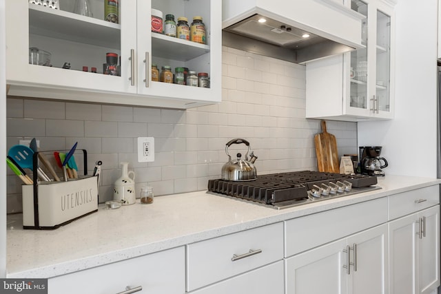 kitchen featuring backsplash, glass insert cabinets, stainless steel gas cooktop, custom exhaust hood, and white cabinetry