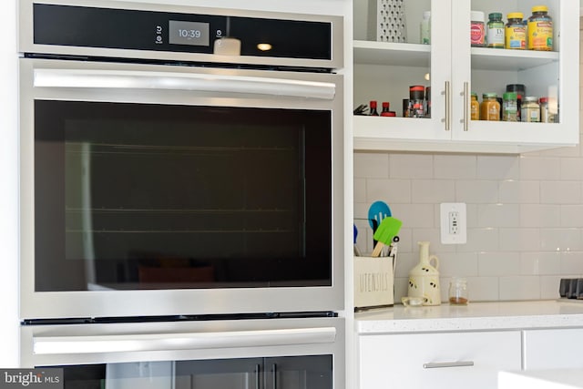 room details featuring oven, tasteful backsplash, white cabinetry, stainless steel oven, and light stone countertops