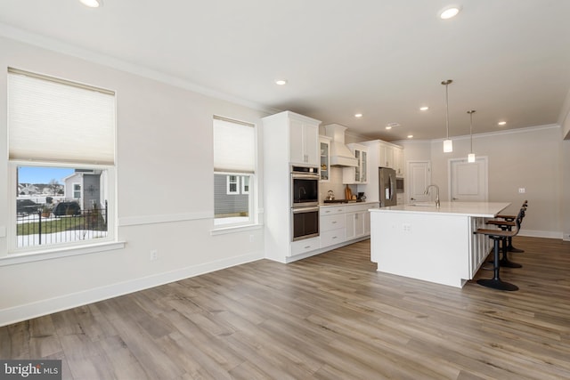 kitchen featuring a kitchen bar, a center island with sink, a sink, wood finished floors, and appliances with stainless steel finishes