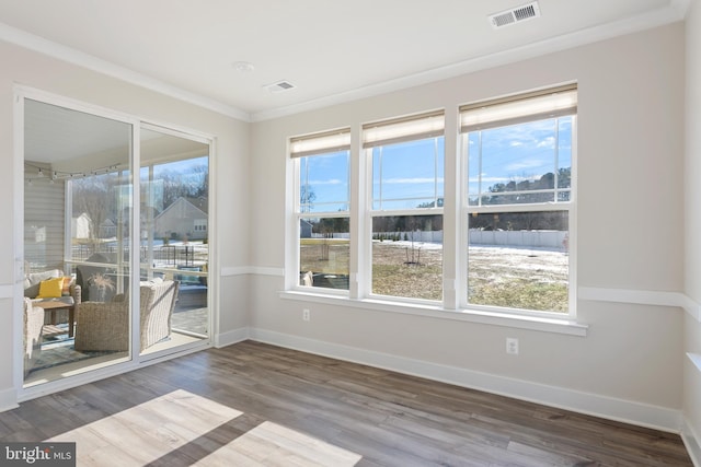 empty room featuring visible vents, crown molding, baseboards, and wood finished floors