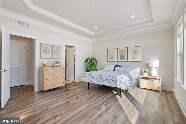 bedroom featuring baseboards, visible vents, ornamental molding, light wood-style floors, and a raised ceiling